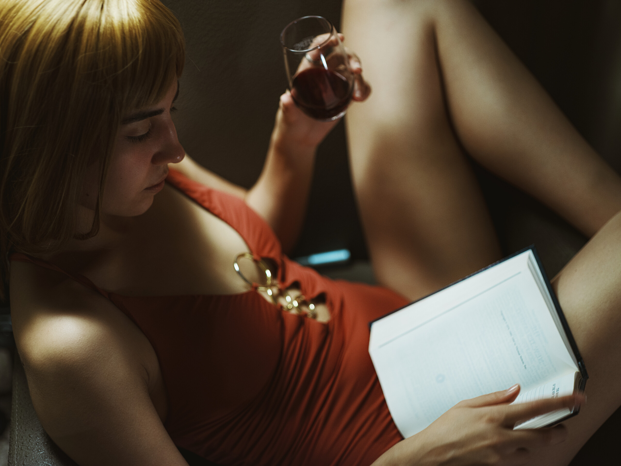 wundervolles junges russisches Model Aliya in rotem Badeanzug posend auf einem Sessel liest die Bibel mit einem Glas wein.